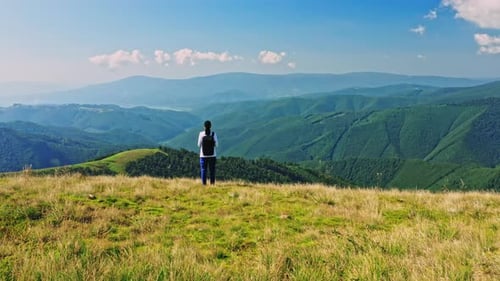 Lone Person Admiring Mountain Vista from Grassy Hilltop