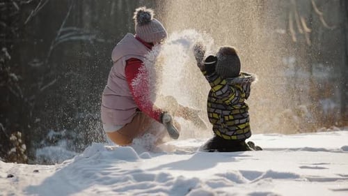 Glückliche Mutter mit kleinem Sohn spielt mit Schnee und wirft ihn hoch
