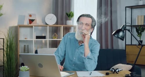 Vieil homme au visage ridé assis devant la caméra et fumant un cigare avec plaisir