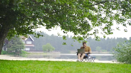 Mann arbeitet mit Laptop im Feld mit Seeblick.