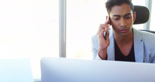 Young Man Talking on Phone at Desk in Office