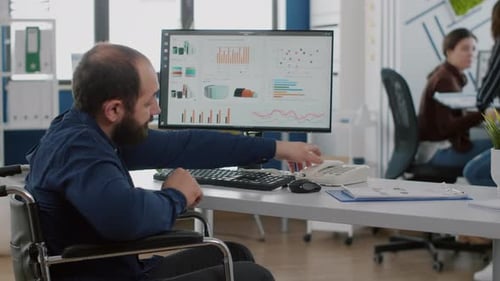 Man in Wheelchair Works at Desk Talking on Phone