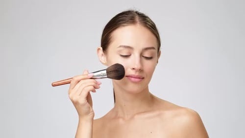Woman Applies Makeup with Brush in Studio