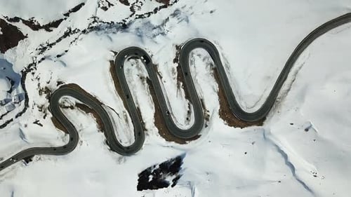 Aerial drone view of a winding road and snow covered mountains in the winter