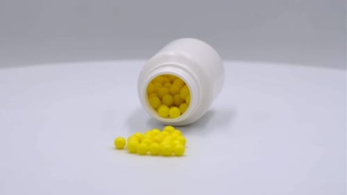 Bottle with Yellow Pills Spilled on White Surface