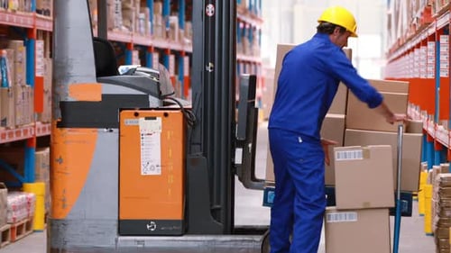 Male warehouse worker arranging stock on forklift truck