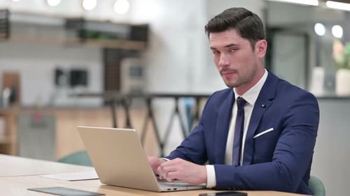 Thumbs Up By Businessman Working on Laptop in Office