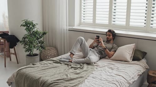 Young Adult Man Relaxing with Mobile Phone on Bed