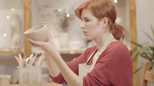 Woman Carefully Inspecting Pottery Bowl in Studio