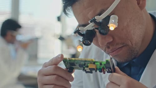 Engineer in Magnifying Glasses Examining Component of Motherboard