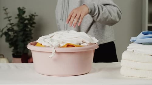 Woman Putting Dirty Clothes Into Basin on Iron Board Closeup Preparing for Washing