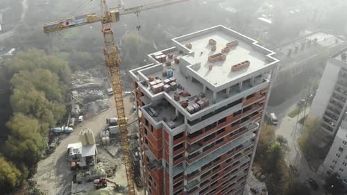 Birds eye view on tower crane in fog standing next to residential building.