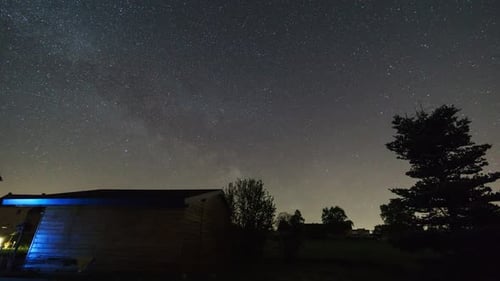 moving milky way on night sky with fir and shed in foreground