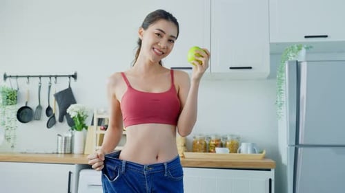 Linda mulher asiática vestindo jeans grandes, sinta-se feliz depois de perder peso para ter saúde em casa.