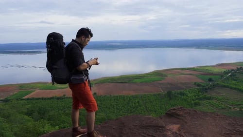 man traveler with backpack using camera taking a photo on the edge of cliff