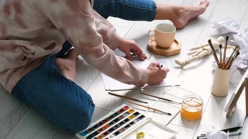 Young Artist Drawing on Floor with Watercolor Supplies