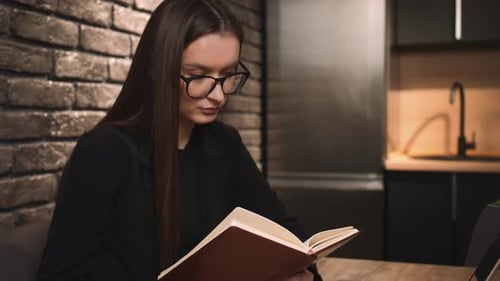 A Young Pretty Woman in Glasses Reading a Book at Home Office