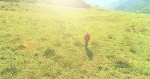 Flight Over Backpack Hiking Tourist Walking Across Green Mountain Field. Huge Rural Valley at Summer