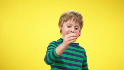 Smiling Boy Plays with Toy Car on Yellow Background