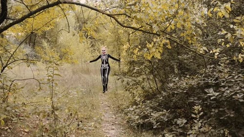 A girl with a scary make-up in a skeleton costume, a mask with rhinestones in a gloomy autumn forest