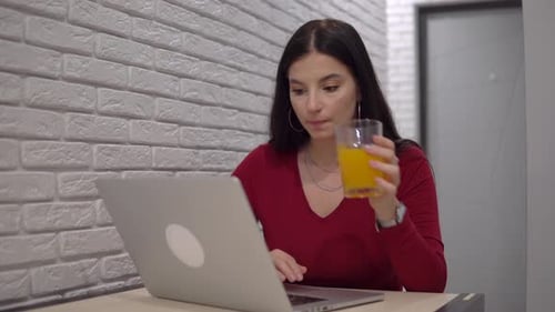 Woman Uses Laptop and Drinks Juice Indoors