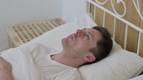 Jeune homme attentionné éveillé dans son lit en pensant
