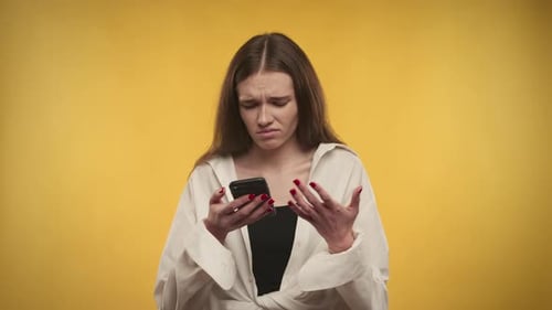 Distraught Woman Using Phone Against Yellow Background