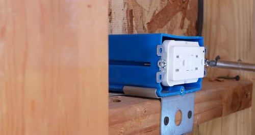 An electrician construction worker using a power drill to re an electrical outlet while remodeling a
