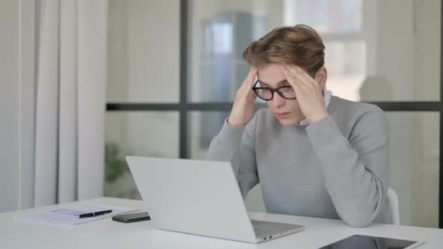 Young Man Having Headache While Working on Laptop in Modern Office