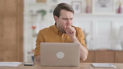 Young Man Coughing while using Laptop in Office