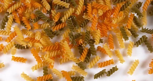 Tri-Color Fusilli Pasta Pouring onto White Surface