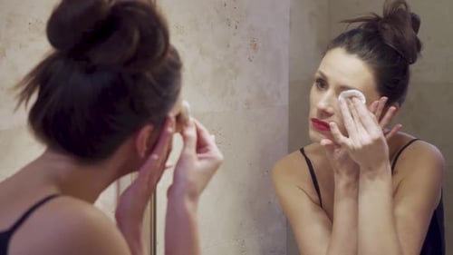 Beautiful Young Woman Doing Makeup Removal in the Mirror