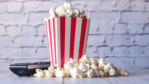 Close Up of Popcorn in a Container and Tv Remote on Table