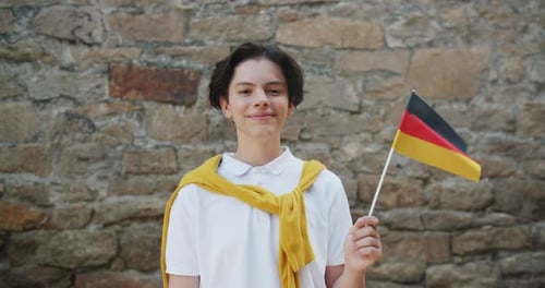 Zeitlupenporträt eines deutschen Jungen, der lächelnd Flagge Deutschlands schwenkt
