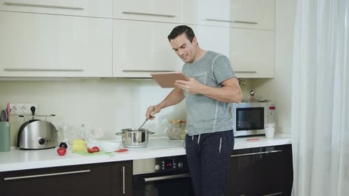 Man Cooking in Kitchen Using Digital Tablet