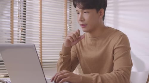 At home, a business asian man types and works online on a desk table with a laptop.