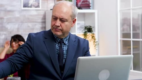 Man Works at Laptop Indoors Puts on Glasses