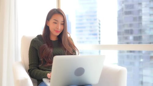 Smiling Woman Typing on Laptop in Urban Apartment