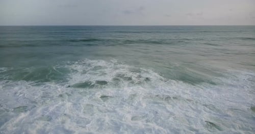 Drone Moving Left Over Big Wild Blue Ocean Waves Reaching the Shore and Crashing Down with White