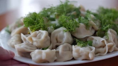 Close Up Sliding Shot of a Plate of Homemade Dumplings with Dill or Herbs on Top and Butter Just