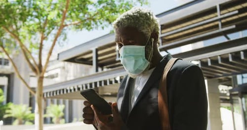 Hombre mayor afroamericano con máscara facial con teléfono inteligente en un parque Corporativa