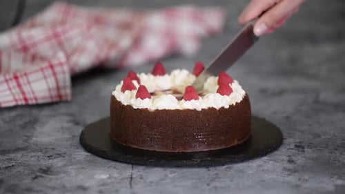 Hand Slicing Chocolate Cake with Cream and Raspberries