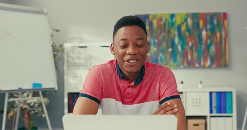 A Young Boy of African American Beauty Sits at Desk in an Office Room with a Laptop Smiles Broadly