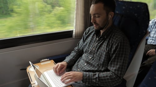 Kreativer Manndesigner, der in einem Zug an seinem Laptop arbeitet.