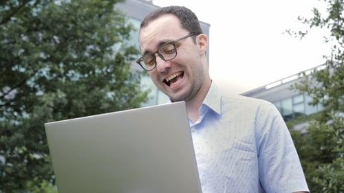 Smiling Man Works on Laptop Outdoors