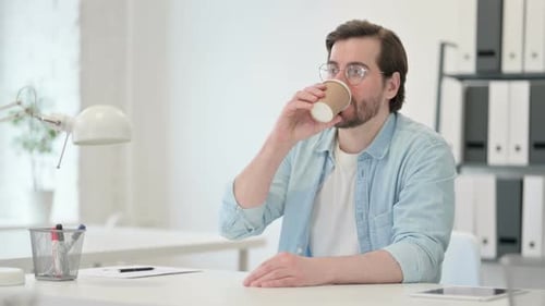 Man Drinking Coffee at Desk in Bright Office
