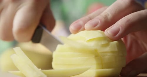 Close Up Of Potato Slicing With A Knife To Cook French Fries With Vegetables On The Background