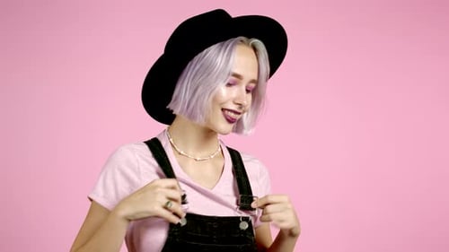 Beautiful Hipster Woman in Hat and Colorful Violet Hairstyle Dancing on Pink Studio Background. Cute