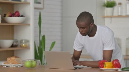 Young Adult Types on a Laptop in Kitchen