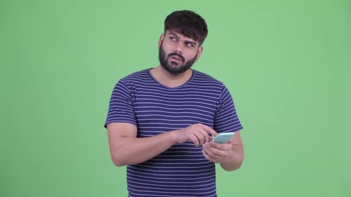Thoughtful Bearded Man Using Mobile Phone Against Green Screen